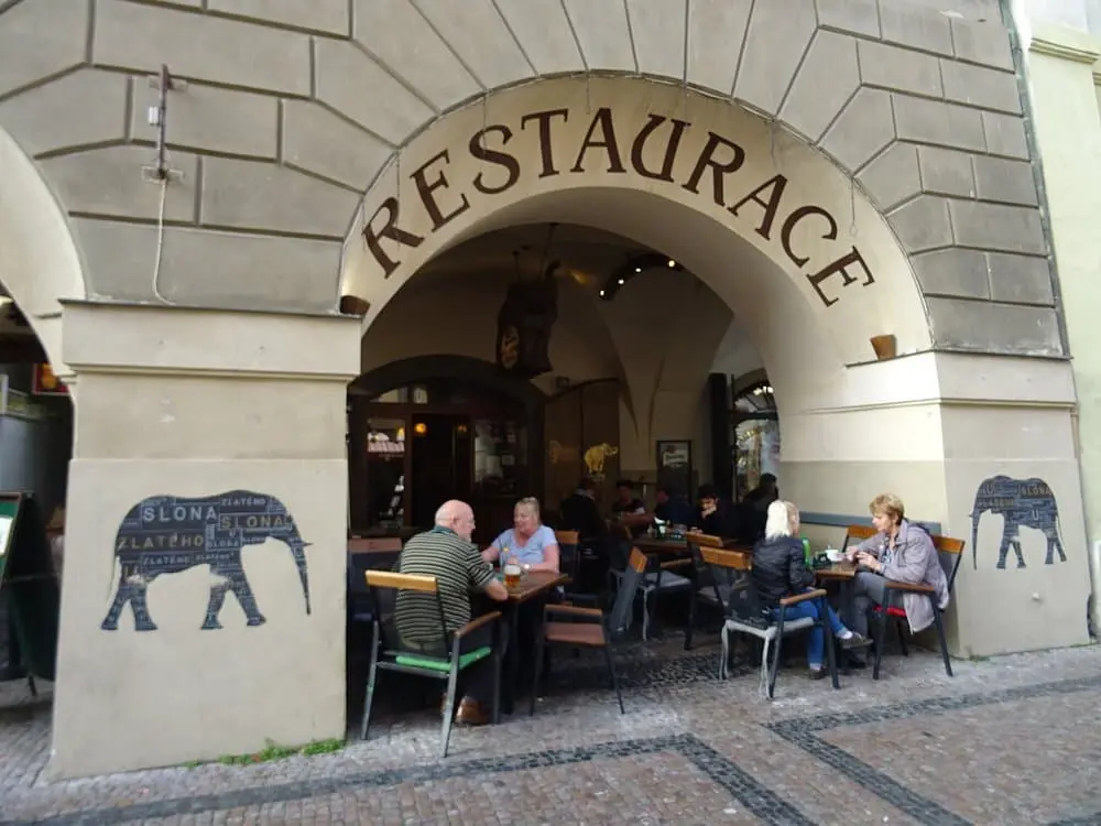 extreriér restaurace u zlatého slona, kde je vidět jak zákaznící sedí u stolu na venkovní terase při letním období, kde jsou sloupy s obrázkem slona