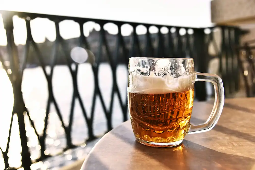 Fotografie piva pilsner urquell na balkonu, kde v pozadí je Praha 