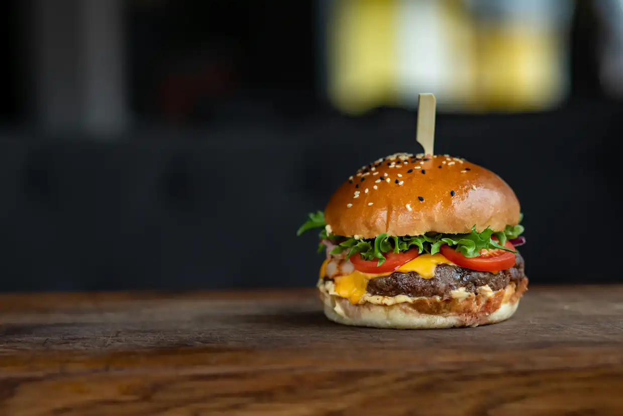 Fotografie burgeru, který je v pravé části obrázku. Burger leží na dřevěném stolku 